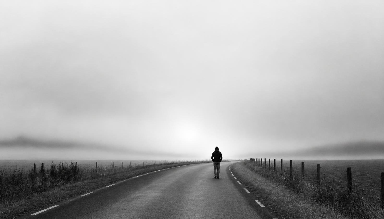 A lone figure walking along an empty road at dawn